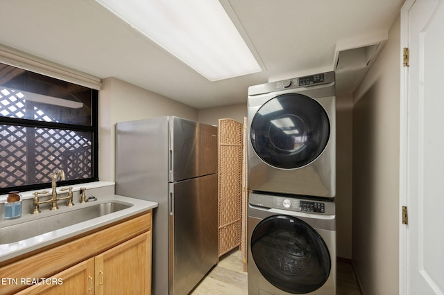 clothes washing area featuring stacked washing maching and dryer, sink, and light wood-type flooring