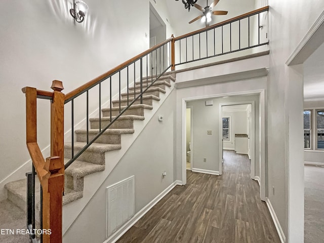 staircase with ceiling fan, a towering ceiling, and wood-type flooring