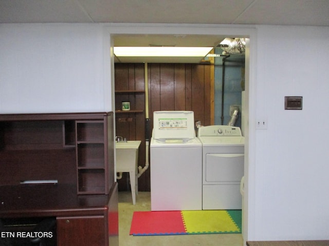 clothes washing area with sink, washing machine and dryer, and wood walls