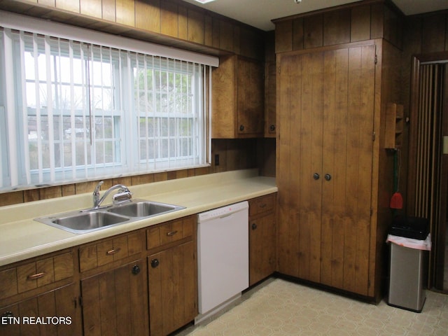 kitchen featuring dishwasher, sink, and wooden walls