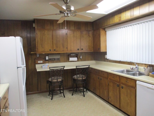 kitchen featuring ceiling fan, sink, wooden walls, and white appliances