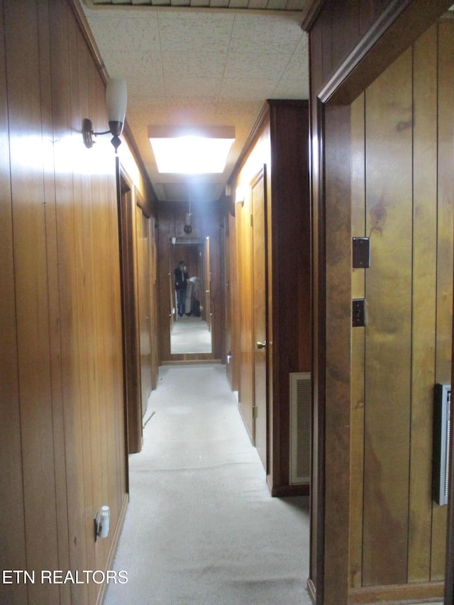 hall with light colored carpet and wooden walls