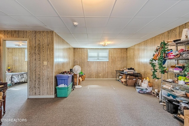 interior space featuring carpet flooring, a drop ceiling, and wooden walls