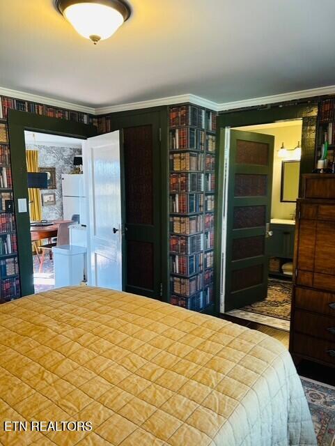 bedroom featuring white refrigerator, crown molding, and ensuite bath