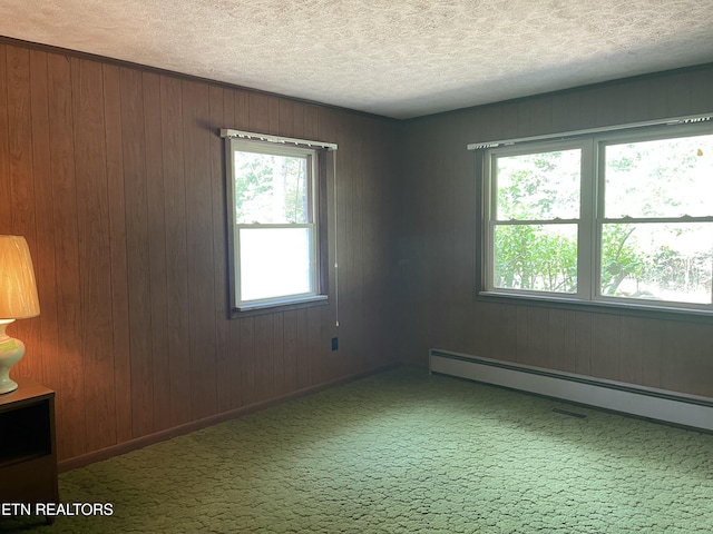 unfurnished room featuring a baseboard heating unit, carpet floors, wooden walls, and a textured ceiling