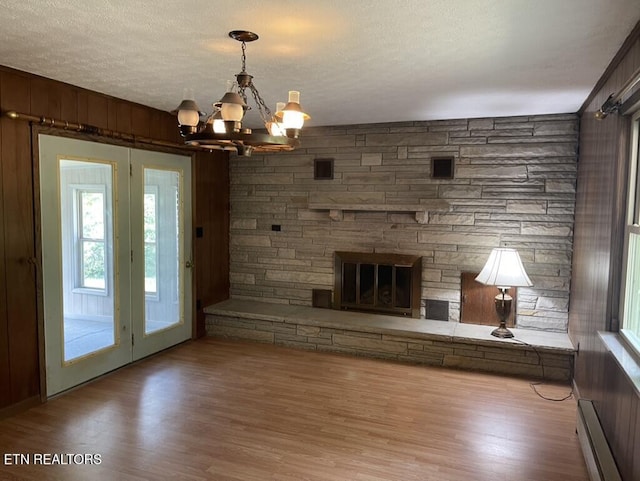 unfurnished living room with a baseboard heating unit, a stone fireplace, a textured ceiling, and hardwood / wood-style flooring