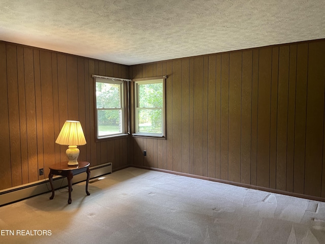 empty room with a baseboard radiator, light colored carpet, a textured ceiling, and wood walls