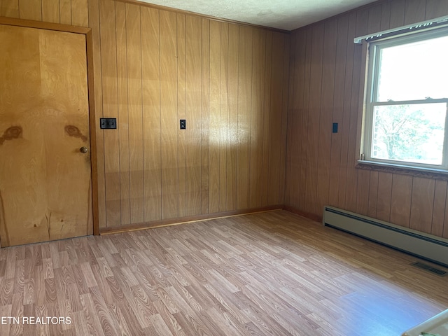 unfurnished room with a baseboard radiator, light hardwood / wood-style floors, and wooden walls