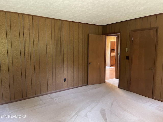 spare room with wooden walls, light colored carpet, and a textured ceiling