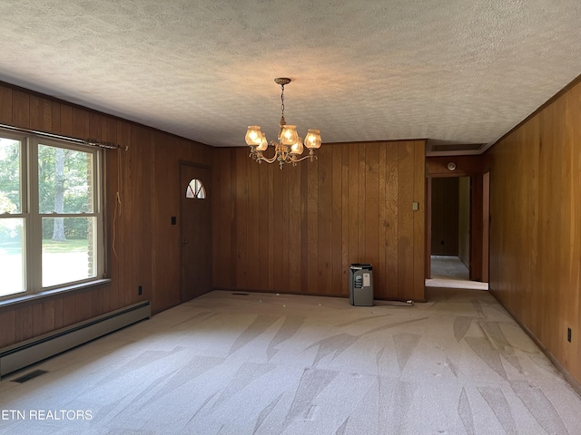 spare room with baseboard heating, an inviting chandelier, wooden walls, a textured ceiling, and light carpet