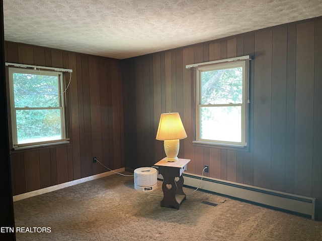 unfurnished room with carpet floors, plenty of natural light, a baseboard heating unit, and a textured ceiling