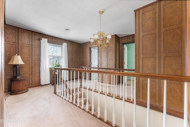 hall with light colored carpet, a chandelier, and a textured ceiling