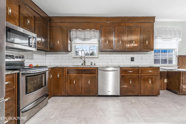 kitchen with sink, dark brown cabinets, light stone countertops, and appliances with stainless steel finishes