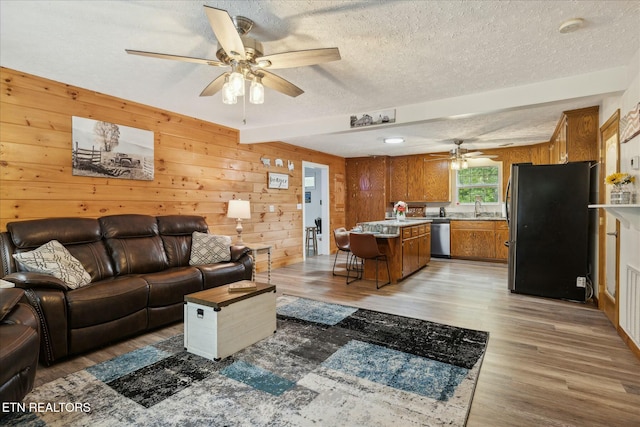 living area featuring light wood-type flooring, wood walls, ceiling fan, and a textured ceiling