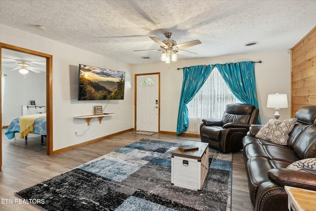 living area with a textured ceiling, wood finished floors, visible vents, a ceiling fan, and baseboards