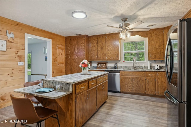 kitchen featuring appliances with stainless steel finishes, light wood-style floors, brown cabinetry, a sink, and a kitchen island