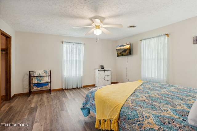 bedroom featuring visible vents, a textured ceiling, baseboards, and wood finished floors