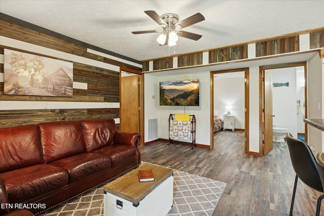 living room with a textured ceiling, ceiling fan, wood walls, wood finished floors, and visible vents