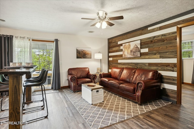 living area featuring a wealth of natural light, wooden walls, wood finished floors, and a textured ceiling