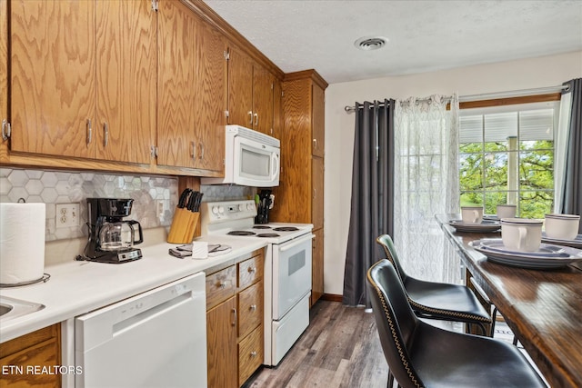 kitchen featuring white appliances, light wood finished floors, visible vents, light countertops, and backsplash