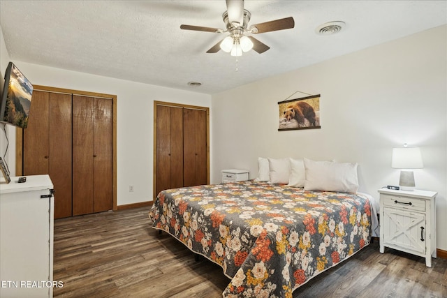 bedroom with wood finished floors, visible vents, baseboards, and two closets