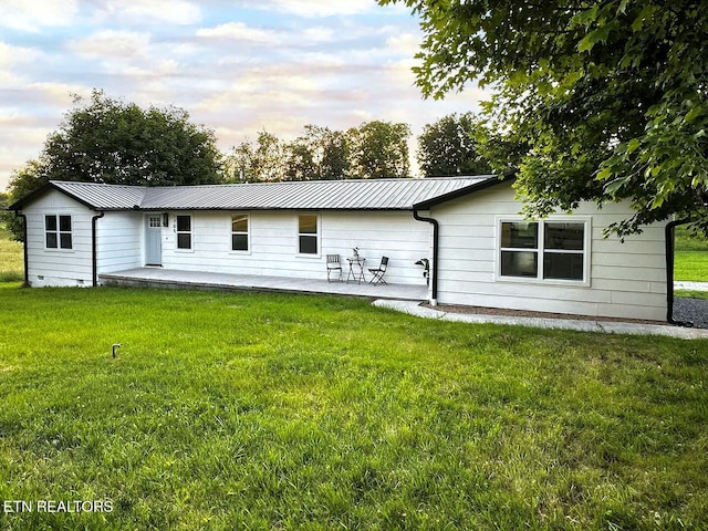 back house at dusk featuring a patio area and a lawn