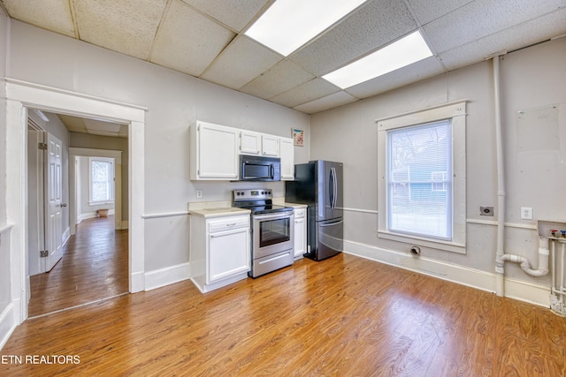 kitchen featuring stainless steel appliances, a drop ceiling, white cabinets, and light hardwood / wood-style flooring