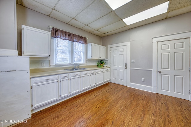 kitchen featuring sink, white fridge, white cabinets, light hardwood / wood-style floors, and a drop ceiling