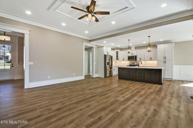 kitchen featuring appliances with stainless steel finishes, decorative light fixtures, white cabinets, ornamental molding, and a kitchen island with sink