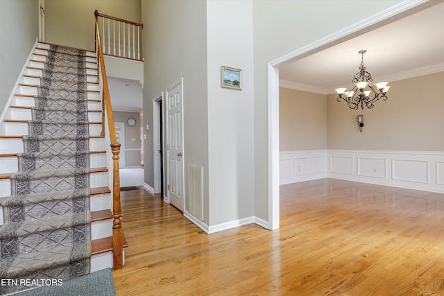 staircase featuring a towering ceiling, wood-type flooring, ornamental molding, and a chandelier