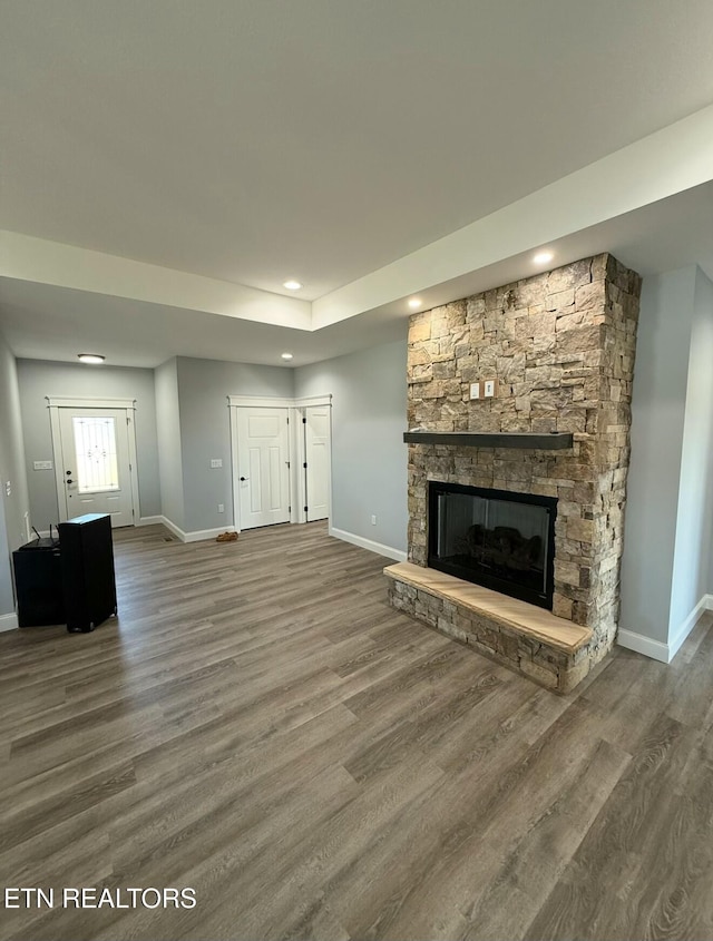 unfurnished living room with a stone fireplace and dark wood-type flooring