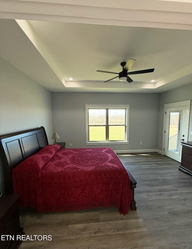 bedroom with a raised ceiling, dark hardwood / wood-style floors, access to exterior, and ceiling fan