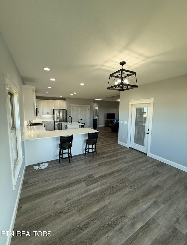 kitchen with dark wood-type flooring, stainless steel fridge, kitchen peninsula, and white cabinets