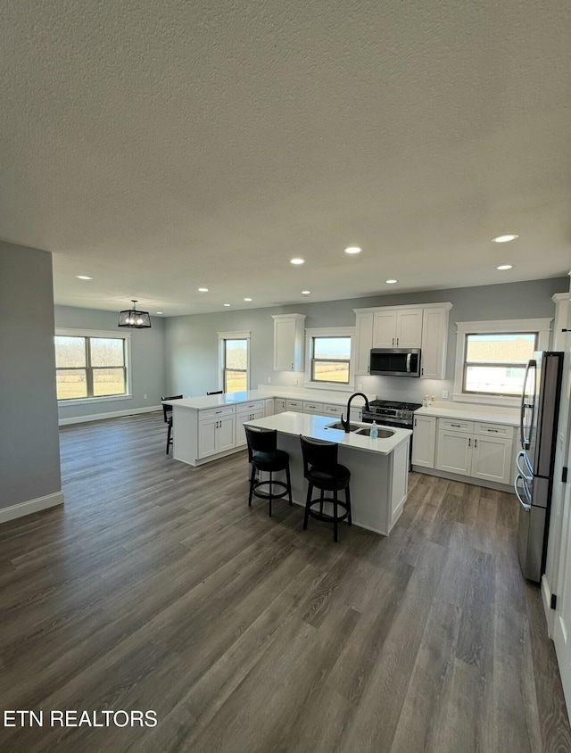 kitchen with a breakfast bar, dark hardwood / wood-style floors, white cabinets, stainless steel appliances, and a center island with sink