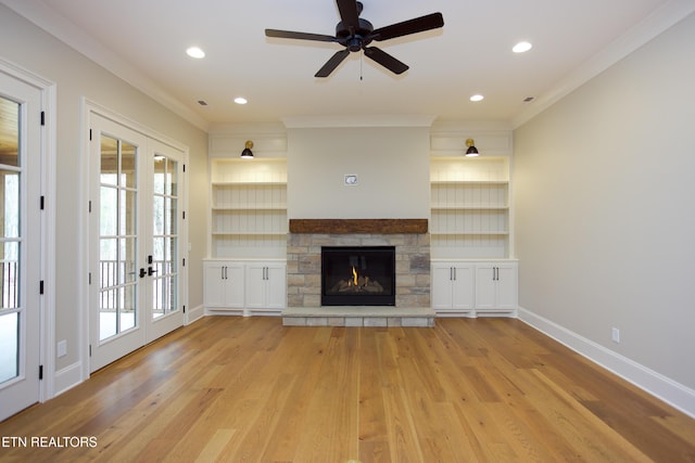 unfurnished living room featuring crown molding, built in features, a fireplace, and light hardwood / wood-style flooring