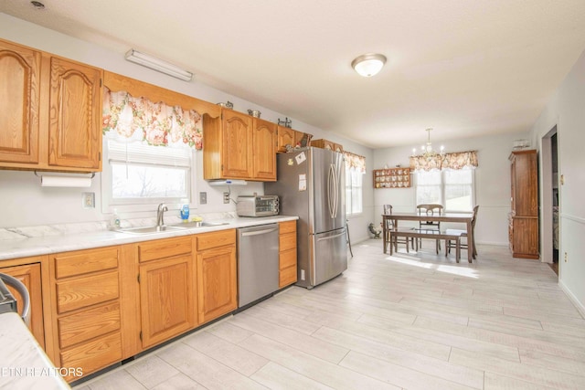 kitchen with sink, hanging light fixtures, appliances with stainless steel finishes, a notable chandelier, and light hardwood / wood-style floors