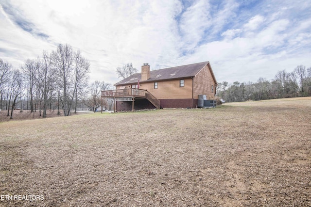 rear view of house with cooling unit, a wooden deck, and a yard