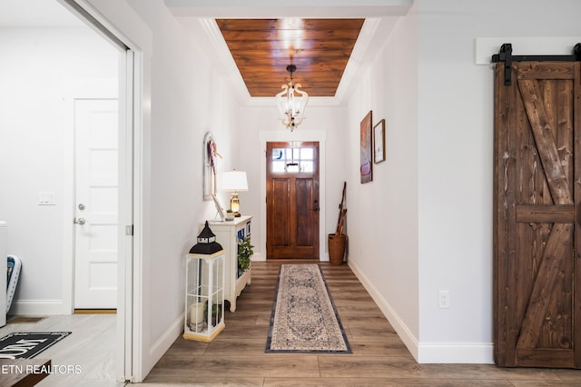 entryway featuring an inviting chandelier, wood-type flooring, ornamental molding, wooden ceiling, and a barn door