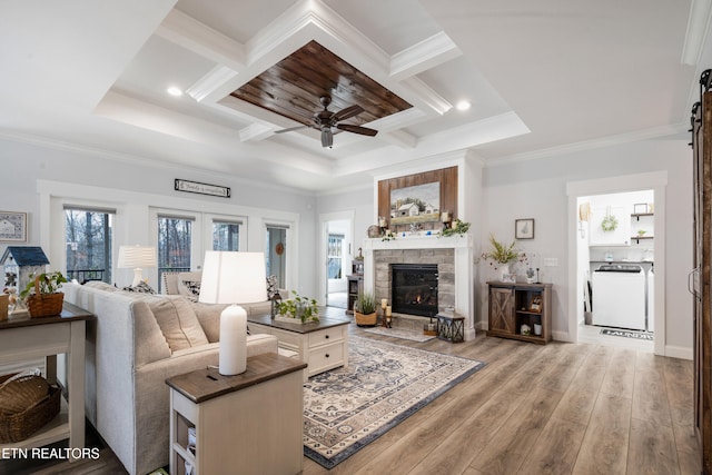 living room featuring ornamental molding, a stone fireplace, washer / dryer, and light hardwood / wood-style floors