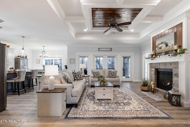 living room with ornamental molding, a fireplace, ceiling fan with notable chandelier, and light wood-type flooring