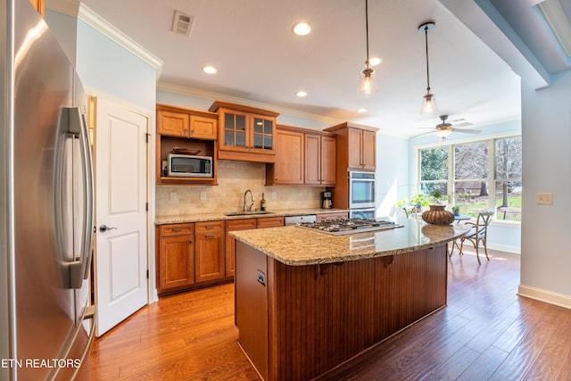 kitchen featuring visible vents, ceiling fan, appliances with stainless steel finishes, brown cabinetry, and a sink