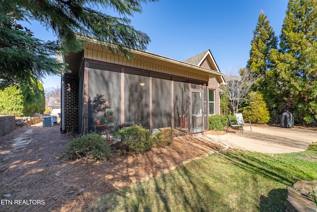 view of property exterior with brick siding, a lawn, cooling unit, a sunroom, and a patio area