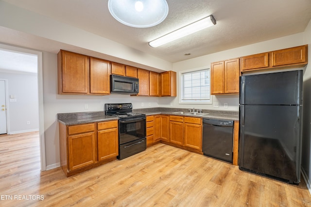 kitchen featuring sink, black appliances, a textured ceiling, and light wood-type flooring