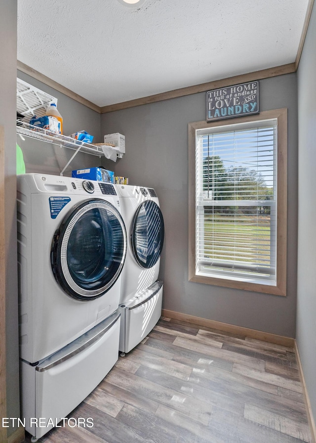 laundry area featuring ornamental molding, light hardwood / wood-style flooring, washing machine and dryer, and a textured ceiling