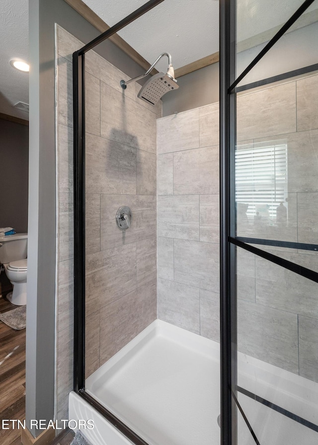 bathroom featuring wood-type flooring, tiled shower, and toilet