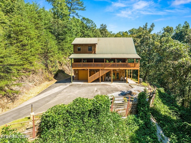 view of front of house with an attached garage, metal roof, driveway, a wooden deck, and stairs