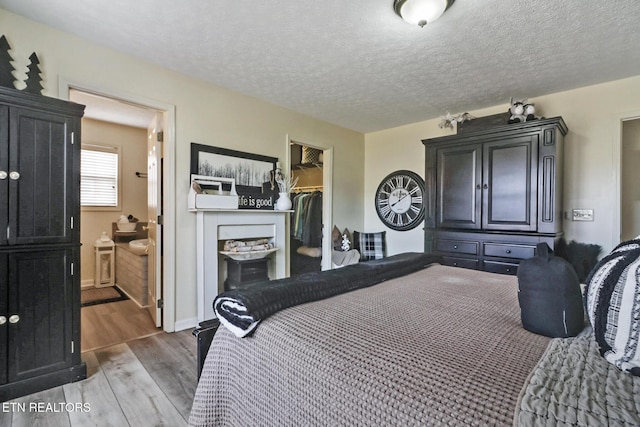 bedroom with ensuite bathroom, a spacious closet, a textured ceiling, a closet, and hardwood / wood-style flooring