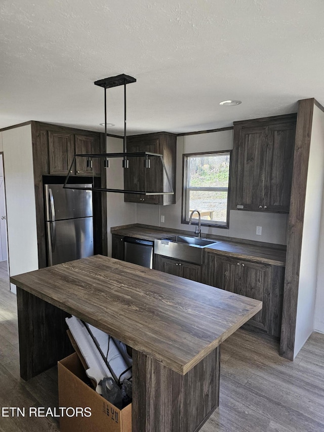 kitchen with pendant lighting, stainless steel appliances, dark brown cabinetry, wood-type flooring, and a kitchen island