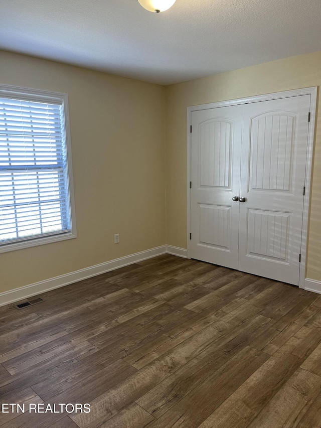 unfurnished bedroom with dark hardwood / wood-style flooring and a closet