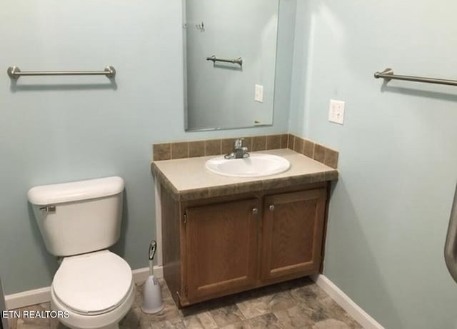 half bath featuring toilet, vanity, and baseboards